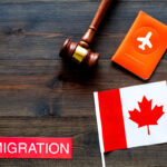 Immigration to Canada concept. Text immigration near passport cover and canadian flag, hammer on dark wooden background top view space for text